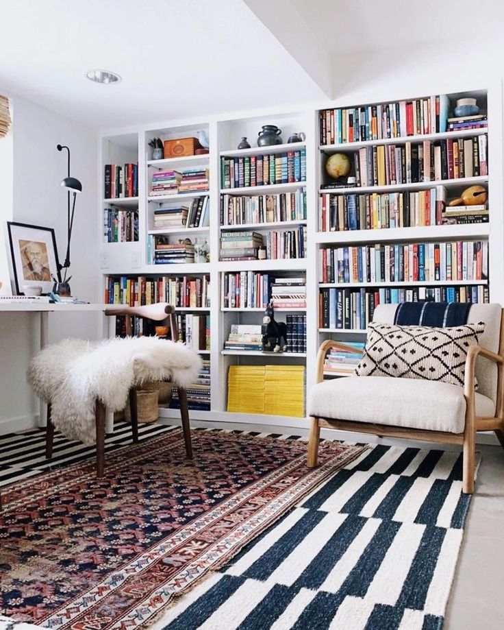 a living room filled with lots of books on top of a white book shelf next to a rug