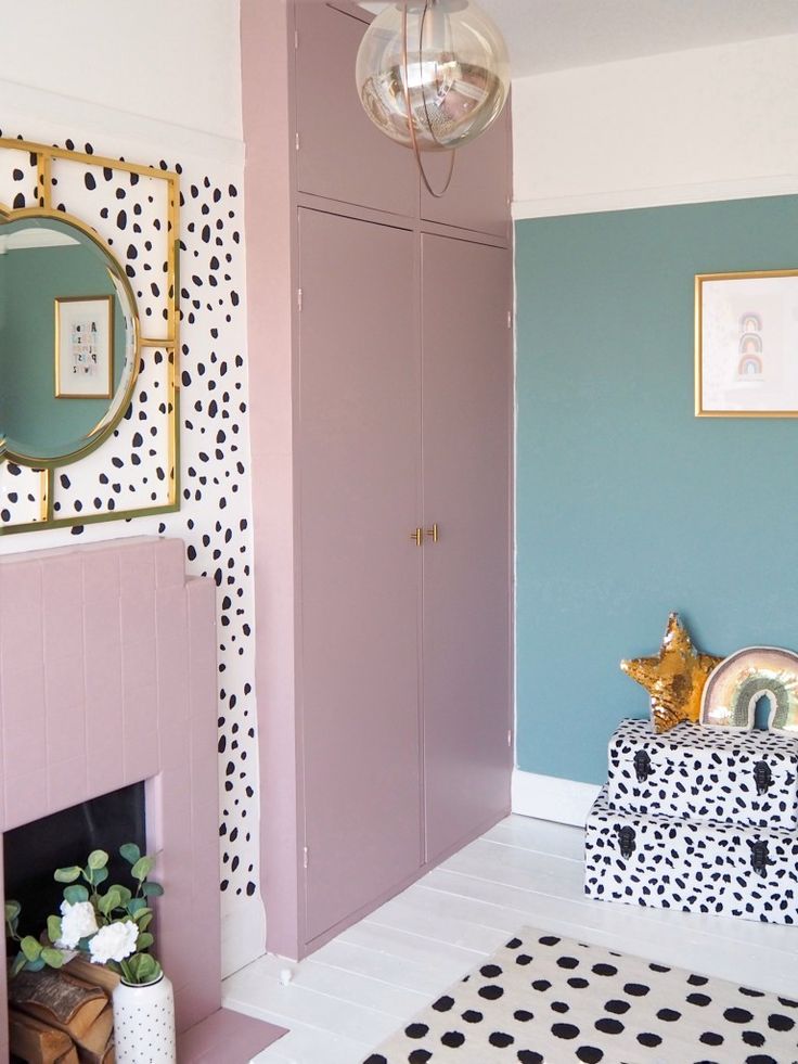 a pink and blue room with polka dots on the walls, a gold framed mirror above a fireplace