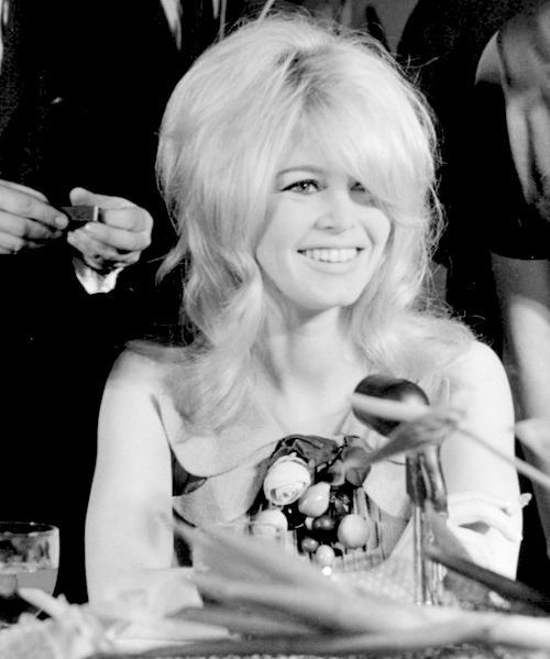 a black and white photo of a woman sitting at a table with other people around her