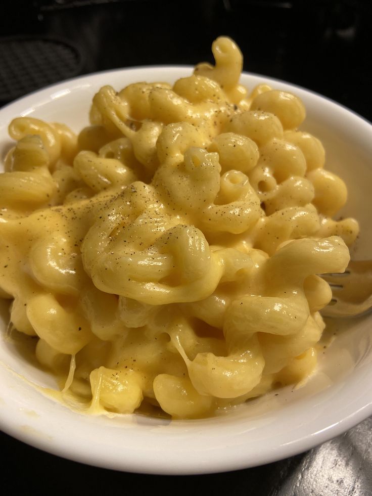 a white bowl filled with macaroni and cheese on top of a black table