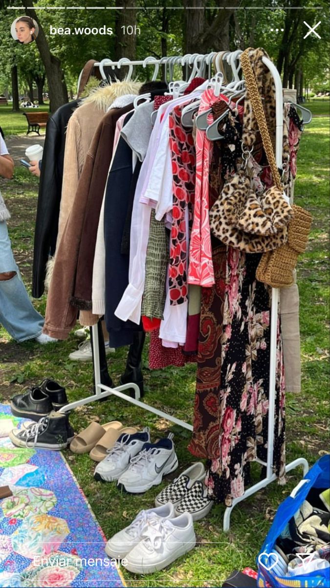 clothes and shoes are hanging on a rack in the grass near a picnic table with an umbrella