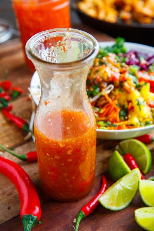 a bottle of sauce sitting on top of a wooden table next to a plate of food