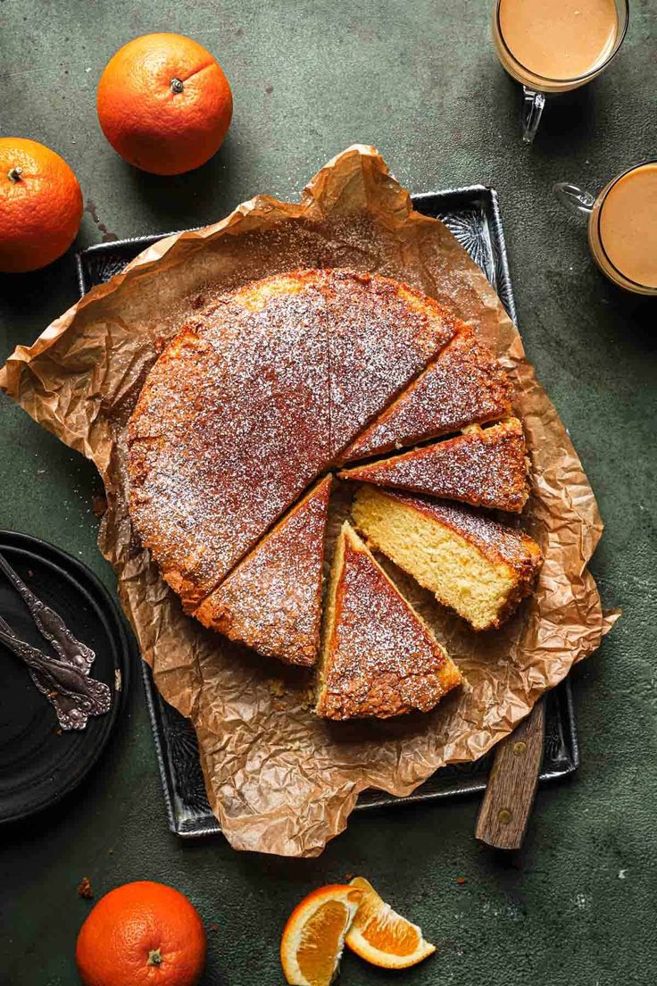 an orange cake with slices cut out on a tray next to some oranges and cups