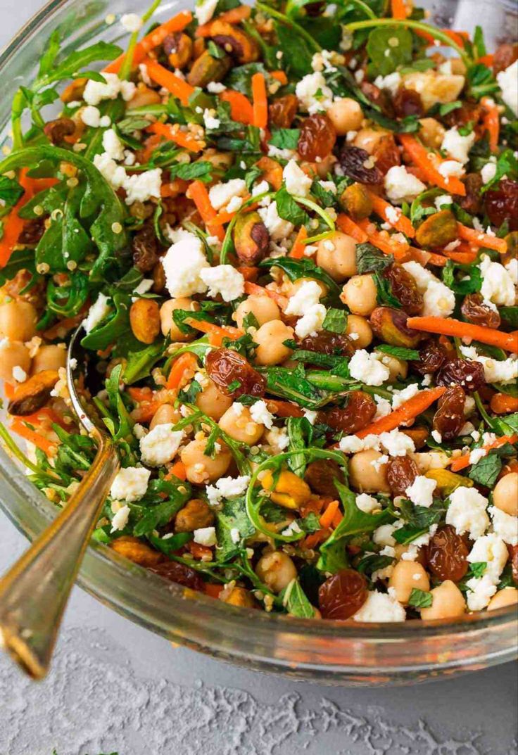 a salad with carrots, spinach and feta cheese in a glass bowl