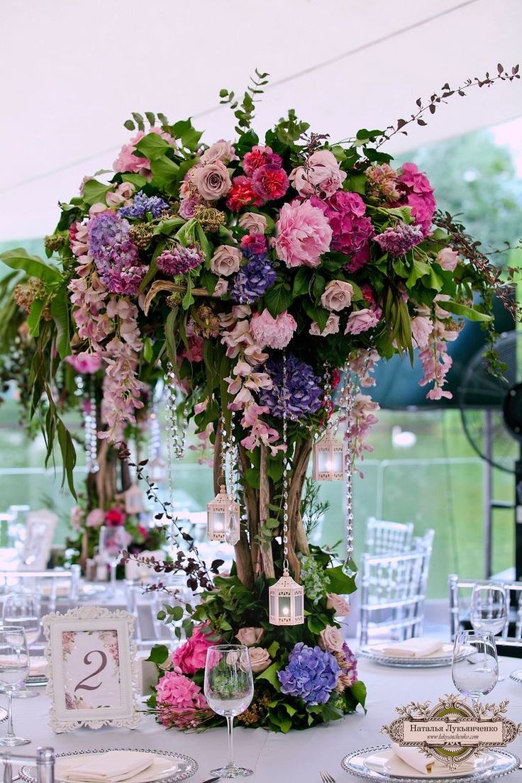 a tall vase filled with pink and purple flowers on top of a white table cloth