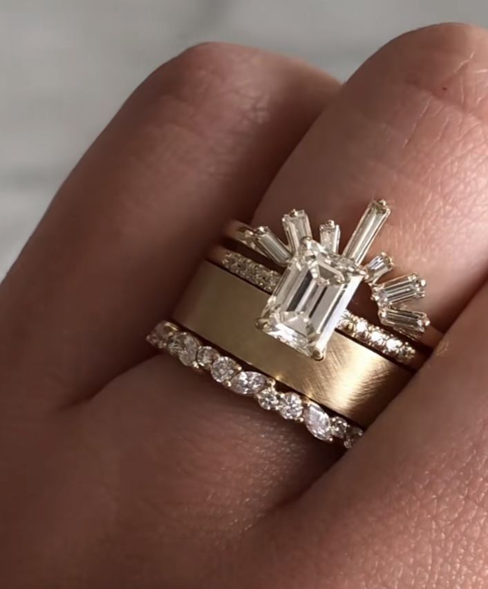 a woman's hand with two gold rings and an emerald ring on top of it