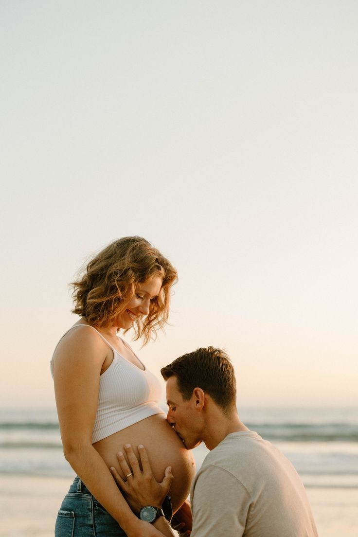 a pregnant woman is holding her husband's belly on the beach