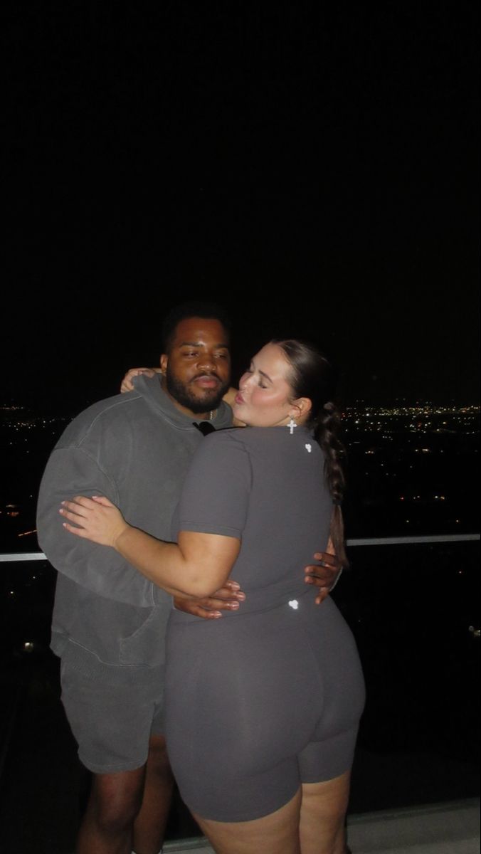 a man and woman hugging each other in front of the city at night