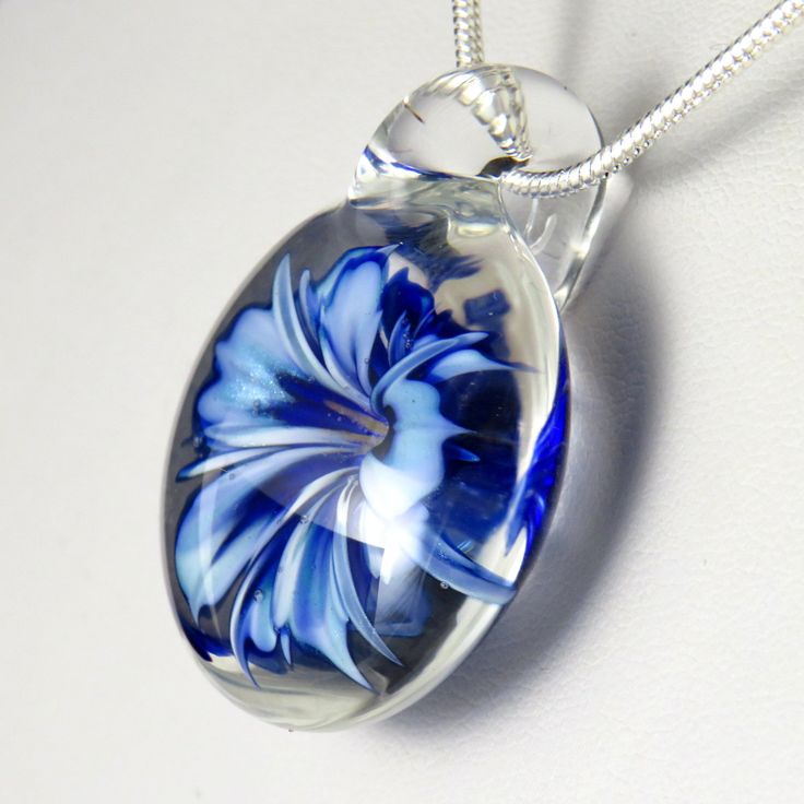 This unusual and unique pendant has a realistic blue and white glass 3D flower inside a solid glass - this isn't resin or a real flower, it's all made entirely of glass! I've used a cobalt blue over white, which I've graduated in tone and to form bands on the petals to make the flower look more realistic, also giving the edges and centre a darker rim of blue. In the centre I've added some yellow 'stamens' to make it look more realistic, where some bubbles have clustered around them to add a dew Blue Flower Necklace For Gifts, Blue Flower Necklace Gift, Blue Flower Pendant Jewelry As Gift, Glass Jewelry With Large Pendant As A Gift, Clear Glass Pendant Jewelry, Blue Flower Pendant Necklace For Gift, Blue Flower Pendant Jewelry Gift, Blue Round Pendant Jewelry With Flower Charm, Clear Glass Flower Jewelry