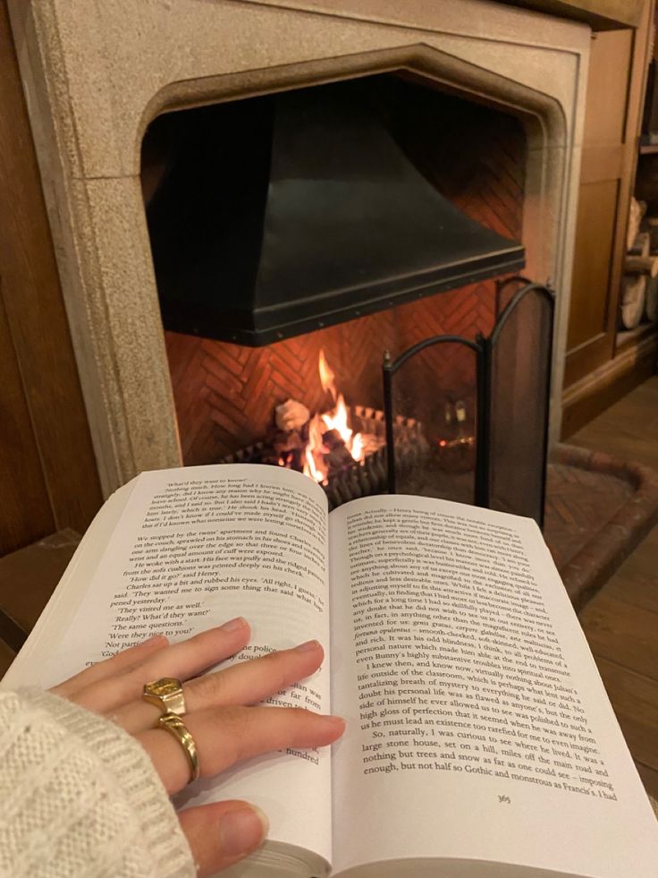 a person reading a book in front of a fire place with their hands resting on an open book