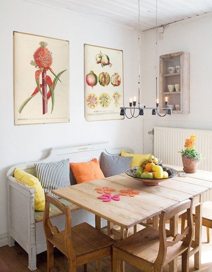 a dining room table with fruit on it in front of two pictures hanging on the wall