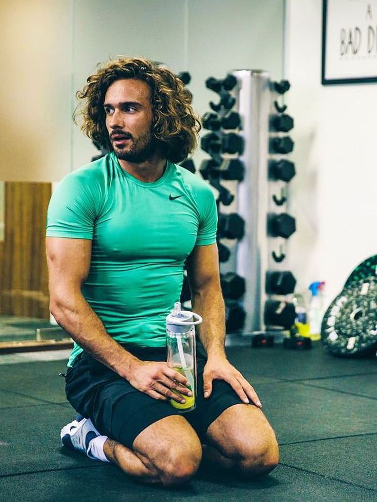 a man with long hair sitting on the floor holding a water bottle