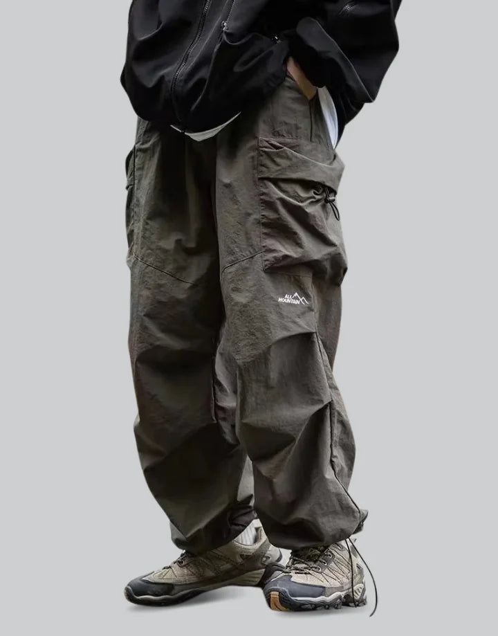 Green Parachute Pants Gray Techwear Cargo Pants For Outdoor, Gray Techwear Pants For Outdoor, Techwear Parachute Pants With Multiple Pockets For Outdoor, Gray Baggy Cargo Pants For Outdoor, Winter Hiking Parachute Pants With Pockets, Gray Techwear Pants For Outdoor Activities, Techwear Pants With Pockets For Outdoor Activities, Techwear Parachute Pants For Outdoor With Pockets, Winter Cargo Pocket Parachute Pants For Outdoor Activities