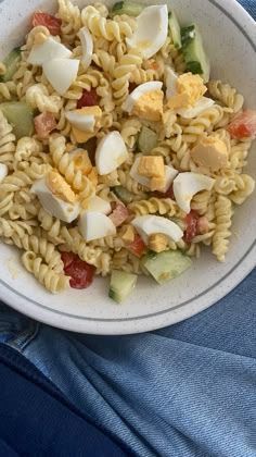 a white bowl filled with pasta salad on top of a blue cloth next to a pair of jeans