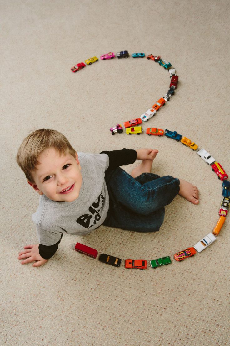 a young boy laying on the floor playing with toy cars