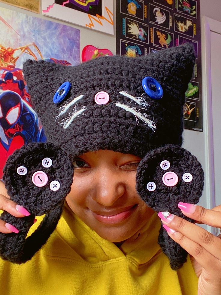 a woman holding up two black crocheted cat mitts in front of her face