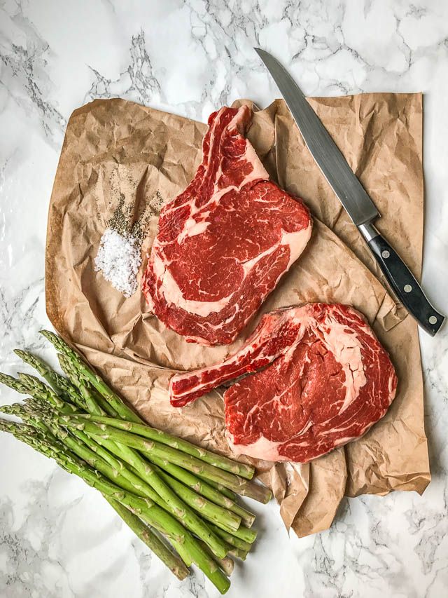 two pieces of raw meat sitting on top of a piece of paper next to asparagus