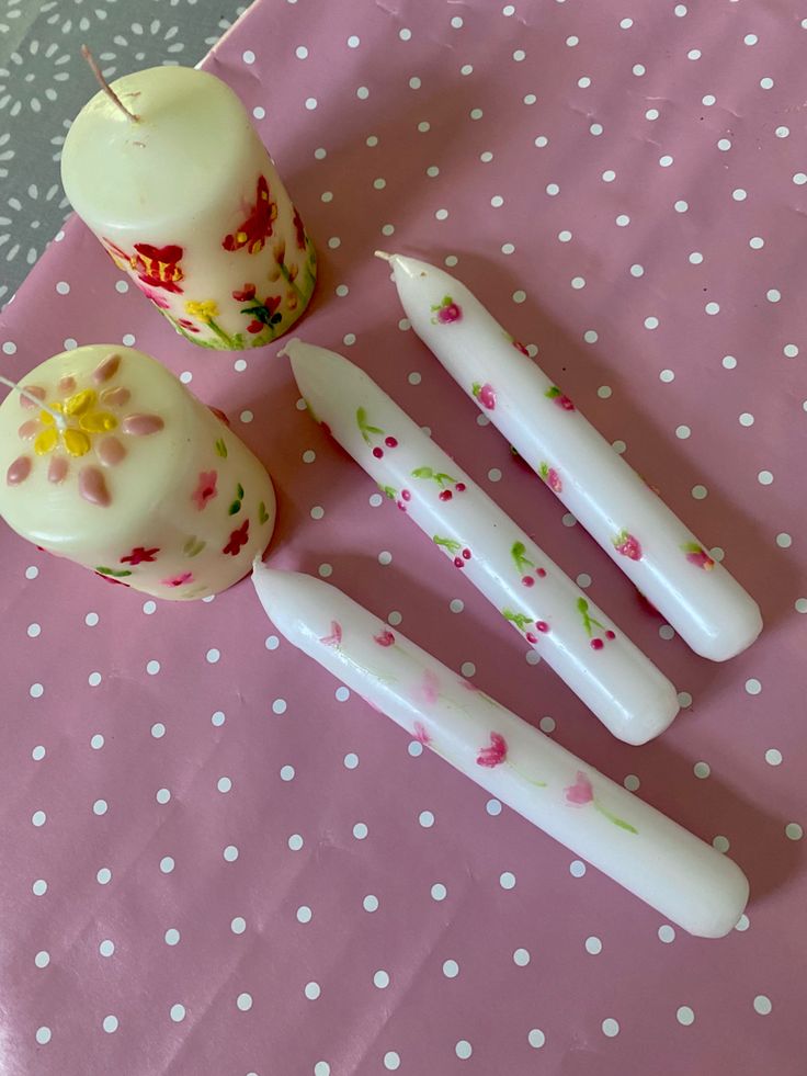 three white candles and one candle holder on a pink tablecloth with polka dot dots