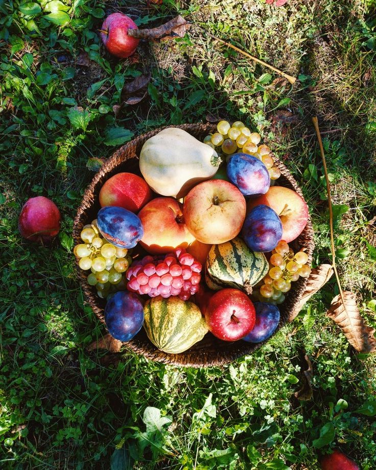 a basket filled with lots of different types of fruit next to some leaves and apples