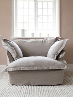 a chair with pillows on top of it in front of a window and white rug