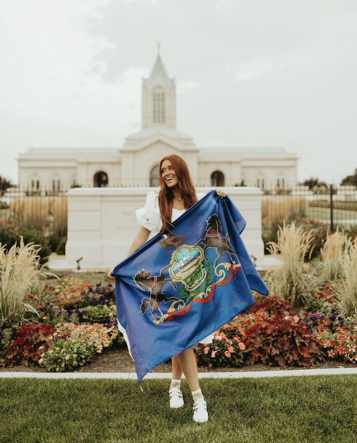 a woman holding a blue flag in front of a white building with a clock tower