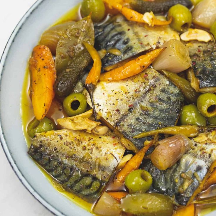 a white plate topped with fish and veggies covered in olives, mustard