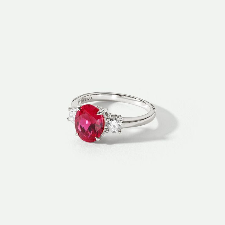 a red and white ring with two diamonds on it's sides, sitting on a white surface