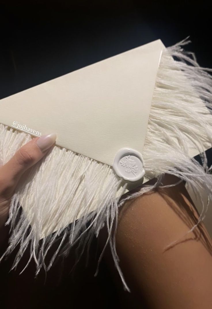 a woman's hand holding an envelope with white feathers and a button on it