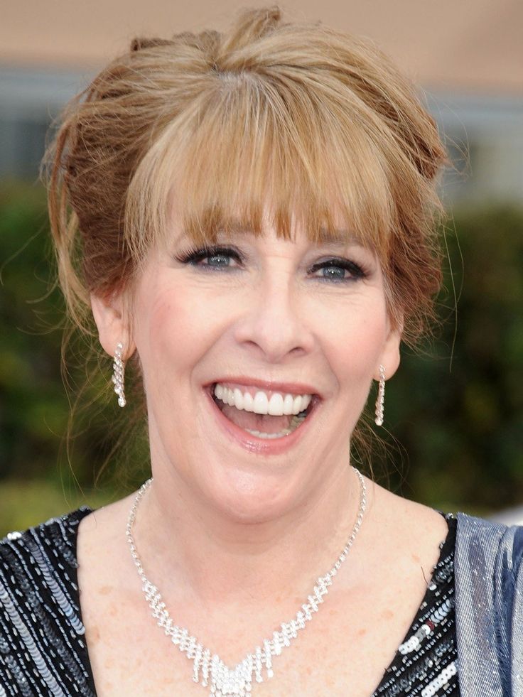 an older woman with blonde hair and blue eyes smiles at the camera while wearing a diamond necklace