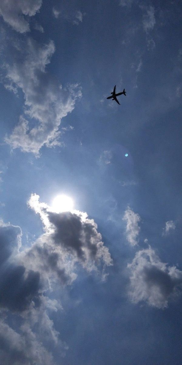 an airplane flying in the sky with clouds and sun shining through it's shadow