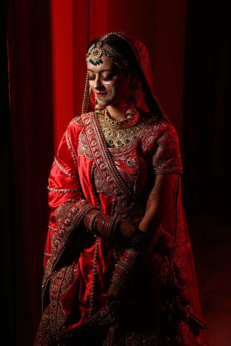 a woman in a red and gold wedding outfit is standing with her hands on her hips