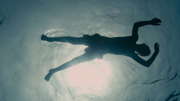 a person is swimming in the water with their shadow on the surface and sun shining through