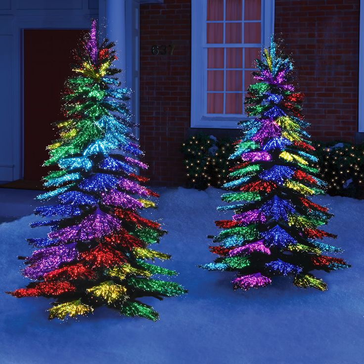 three christmas trees in front of a house decorated for the holiday season with lights on them