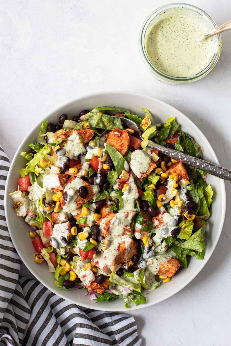 a white bowl filled with salad and dressing next to a glass of dressing on the side