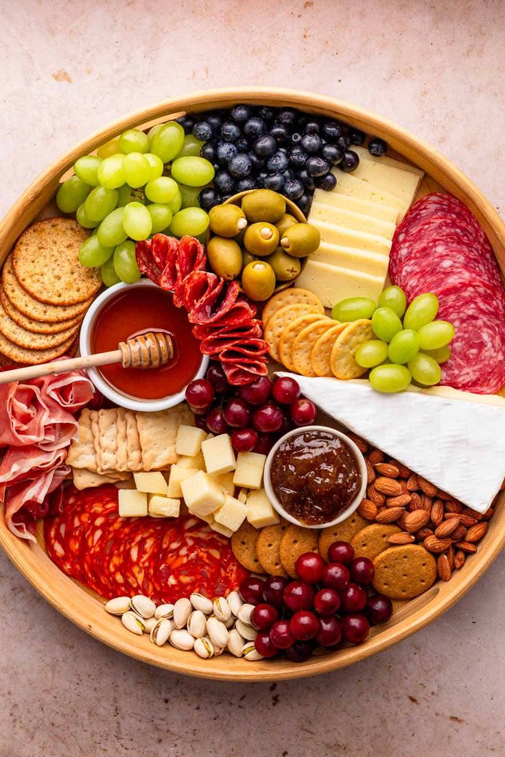 a platter filled with cheese, crackers, grapes, meats and nuts