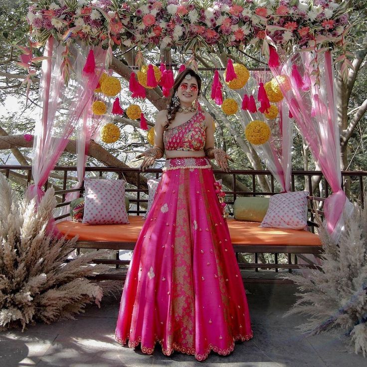 a woman in a pink and yellow dress standing under a canopy with flowers on it