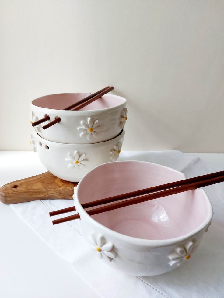 three bowls with chopsticks in them on a white tablecloth next to each other