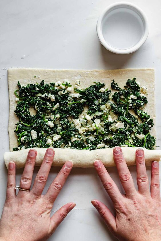 two hands on top of a pizza dough with spinach and fettuccine