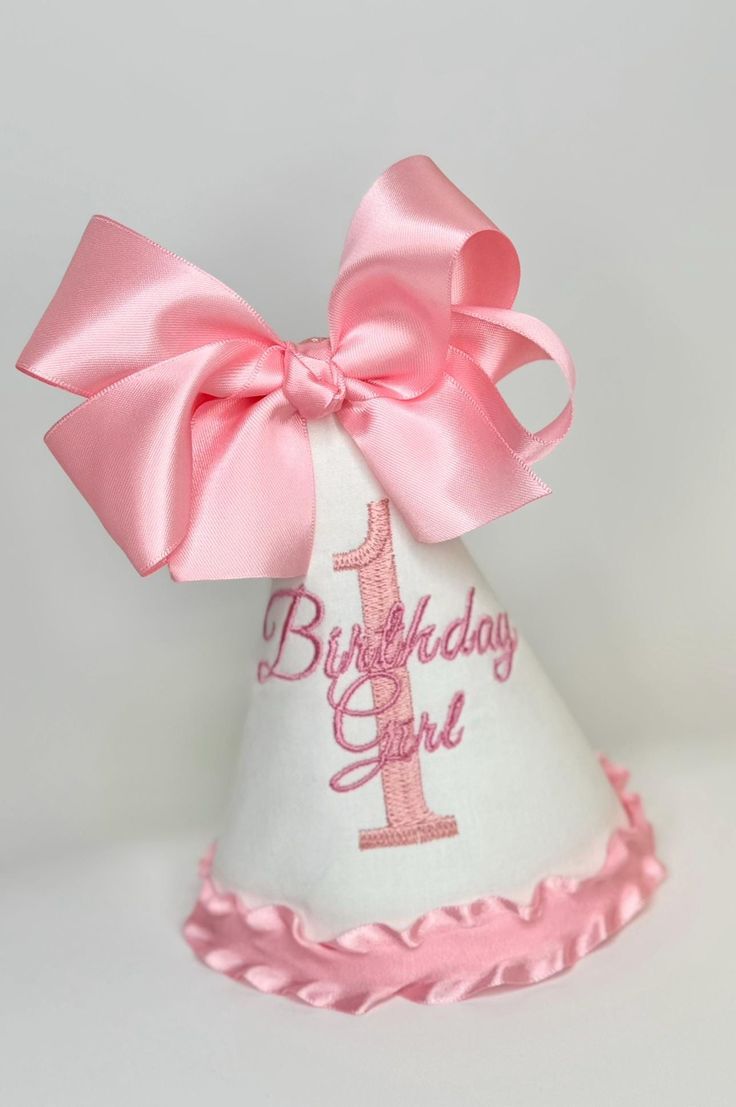 a white birthday hat with pink ribbon and a number 1 on the side, decorated with a large pink bow