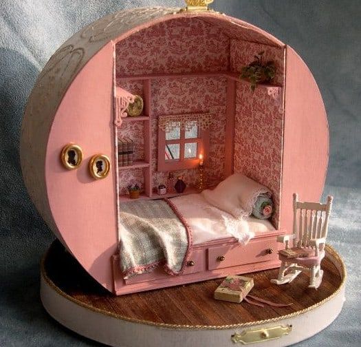 a doll house with a bed and chair in the middle on a wooden table next to a gray background