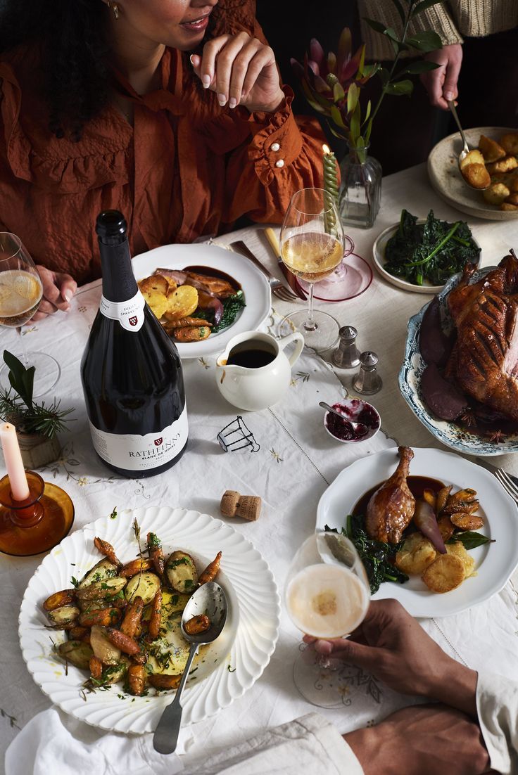 a woman sitting at a table with plates of food and wine in front of her