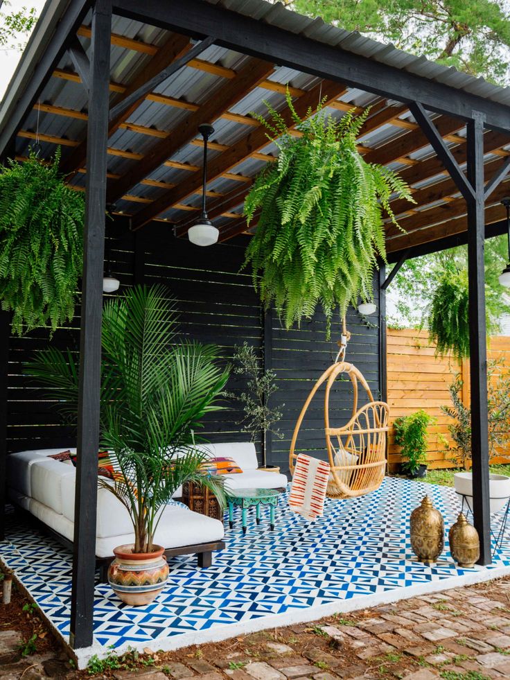 a covered patio with hanging chairs and potted plants on the side, surrounded by brick pavers