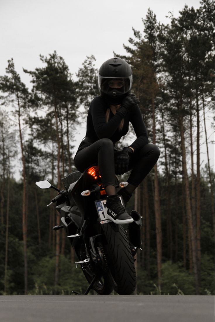 a person riding on the back of a motorcycle in front of some tall pine trees