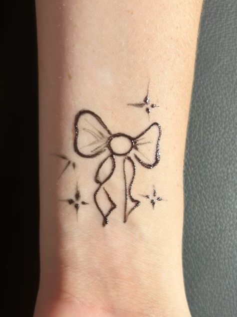 a small tattoo on the wrist of a woman with a bow and stars around it