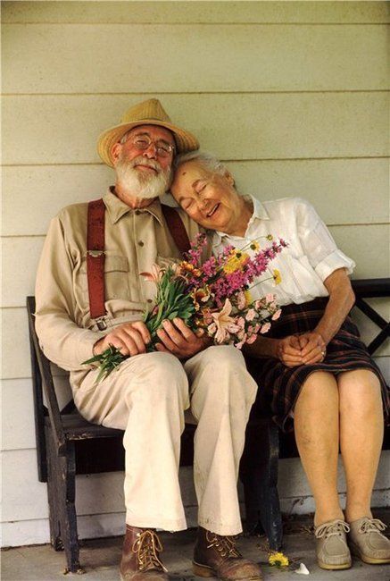 an older couple sitting on a bench with flowers