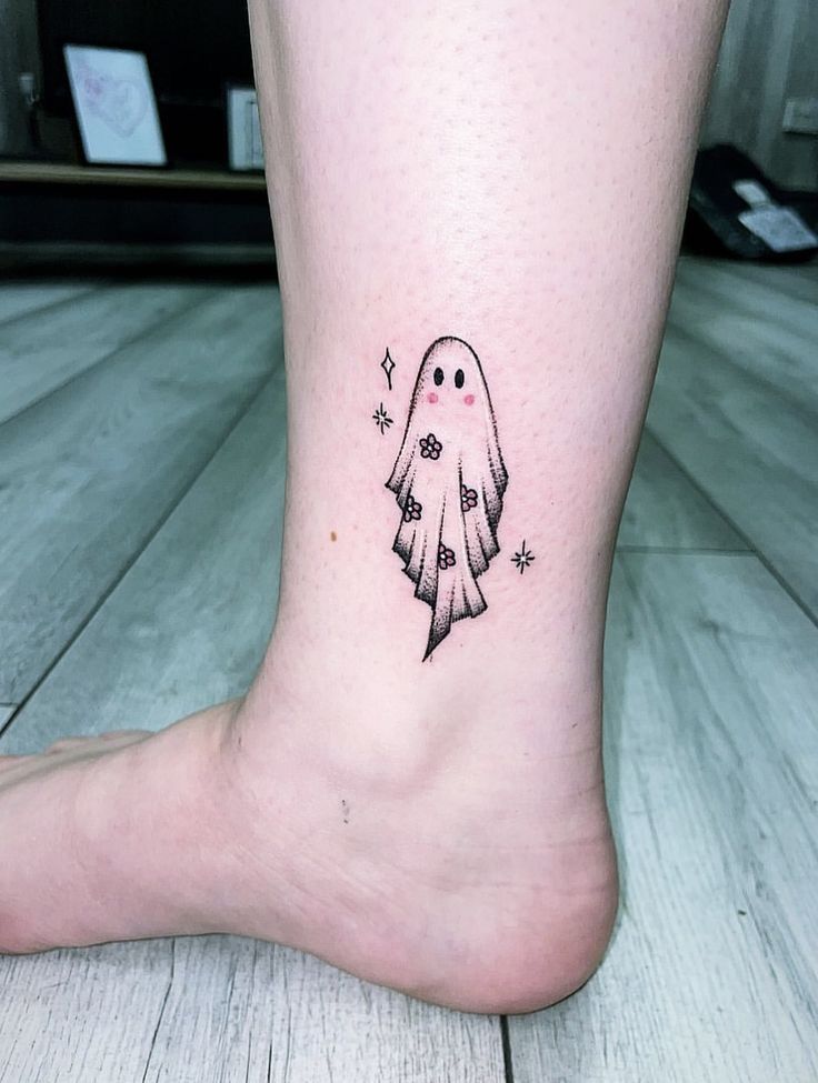 a small black and white ghost tattoo on the ankle, with stars coming out of it