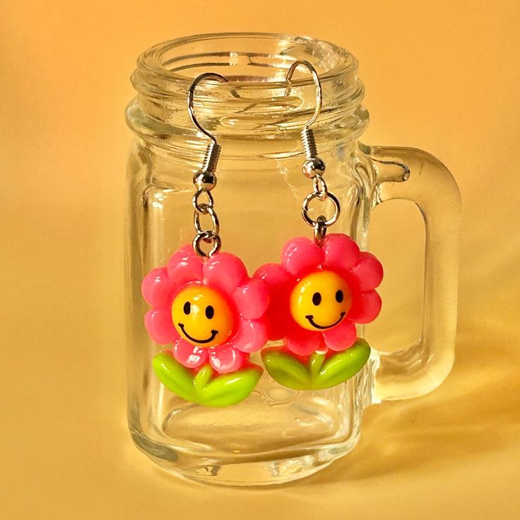 two plastic flowers are hanging from the handle of a glass mug with a smiley face on it