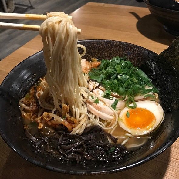 a black bowl filled with noodles, meat and veggies next to chopsticks