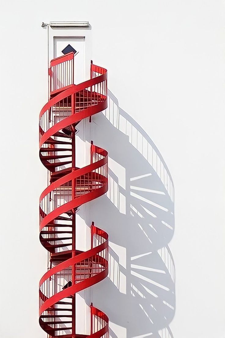 a tall red spiral staircase next to a white wall