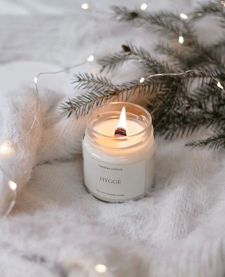 a lit candle sitting on top of a white blanket next to a christmas tree branch